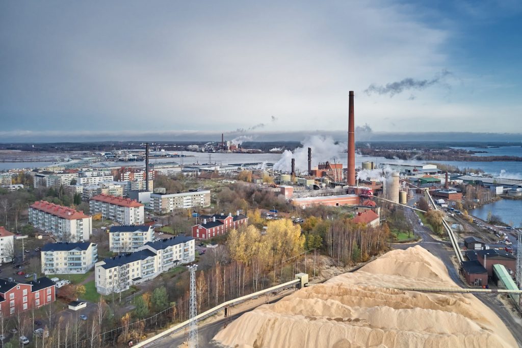 Kotkan kaupunkia kuvattuna ylhäältä päin. Kuvassa tehtaan piippu, kerrostaloja ja merimaisemaa.