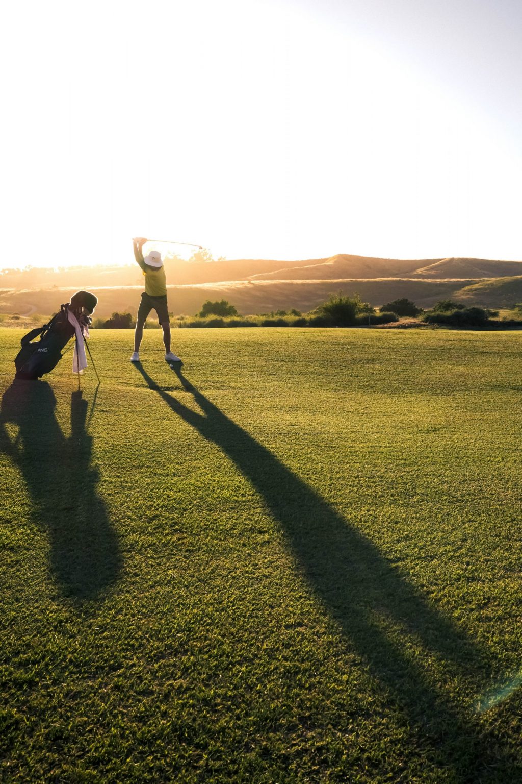 Golf-viheriö ja ihminen pelaamassa golfia auringonlaskussa.